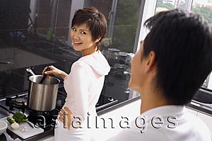 Asia Images Group - Woman cooking on stove, looking over shoulder at man standing behind her