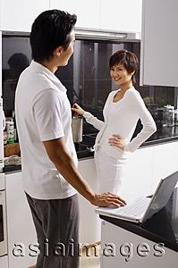 Asia Images Group - Woman cooking on stove, man with laptop, looking at each other