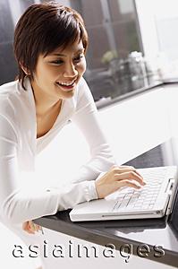 Asia Images Group - Young woman leaning on kitchen counter, using laptop