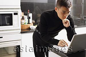 Asia Images Group - Man in kitchen, looking at laptop