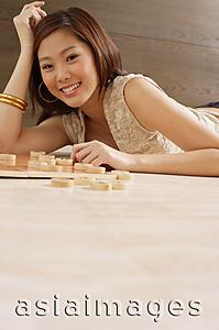 Asia Images Group - Woman lying on floor, hand on head, Chinese chess pieces on floor next to her
