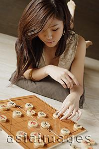 Asia Images Group - Woman lying on floor, playing with Chinese chess board