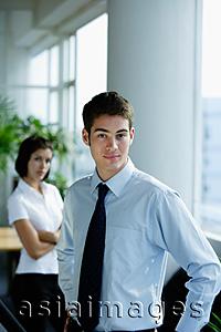 Asia Images Group - Male executive with hands on hips, looking at camera, woman in the background