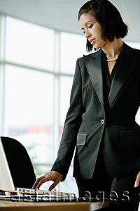 Asia Images Group - Businesswoman dressed in black, standing, looking at laptop on desk
