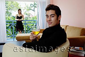 Asia Images Group - Man sitting in armchair in living room, holding a glass of wine, smiling, woman in the background