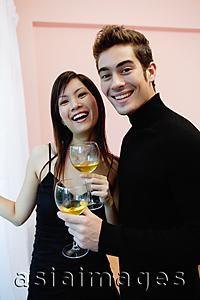 Asia Images Group - Couple holding wine glasses, standing side by side, smiling at camera