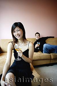 Asia Images Group - Woman in black dress holding wine glass, smiling at camera, man in the background