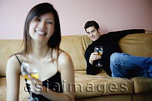 Asia Images Group - Couple sitting apart in living room, both looking at camera, focus on the man in the background