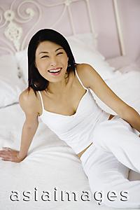 Asia Images Group - Woman sitting on bed, smiling at camera