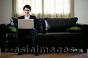 Asia Images Group - Man seating on sofa, using laptop
