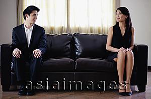 Asia Images Group - Man and woman sitting apart on sofa, turning to look at each other