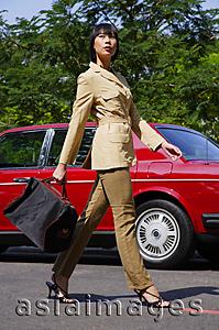 Asia Images Group - Woman walking by red car, carrying bag