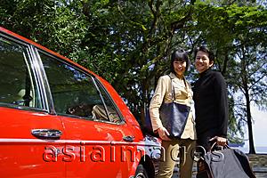 Asia Images Group - Couple carrying bags, standing next to red car, smiling at camera