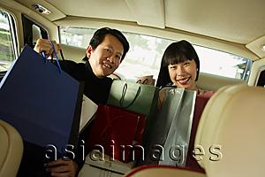 Asia Images Group - Couple sitting in backseat of car, shopping bags on their laps