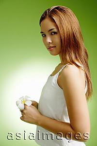 Asia Images Group - Young woman holding Frangipani flower, looking at camera