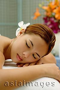 Asia Images Group - Young woman with flower in hair, lying on massage table, eyes closed