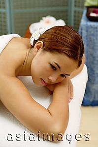 Asia Images Group - Young woman with flower in hair, lying on massage table, leaning on arms