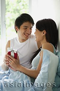 Asia Images Group - Couple in bed face to face, man giving woman present