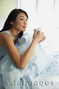Asia Images Group - Woman sitting up in bed, holding cup