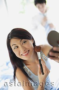 Asia Images Group - Woman applying make-up, looking at compact