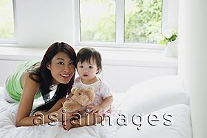 Asia Images Group - Young girl sitting on bed, mother leaning next to her, smiling at camera