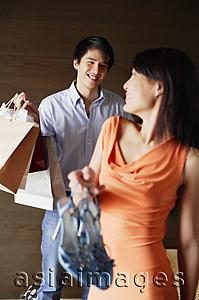 Asia Images Group - Woman holding shoes, looking over shoulder at man carrying shopping bags