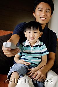 Asia Images Group - Father with young son on lap, holding TV remote control