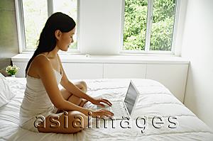Asia Images Group - Woman sitting on bed, using laptop