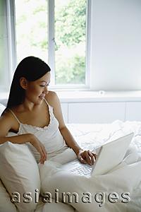Asia Images Group - Woman on bed, using laptop