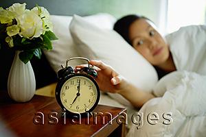 Asia Images Group - Woman lying in bed, reaching for alarm clock on bedside table