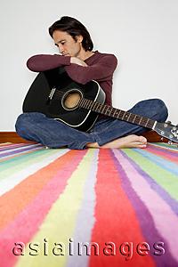 Asia Images Group - Man holding guitar, sitting cross-legged on floor, looking down