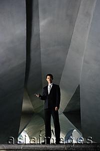 Asia Images Group - Businessman standing in tunnel, holding mobile phone, smiling at camera