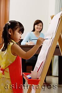 Asia Images Group - Young girl painting on easel, mother in the background