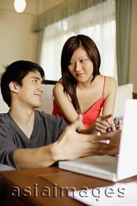 Asia Images Group - Couple in living room, with laptop and calculator, discussing expenses