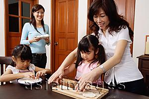 Asia Images Group - Family of females in kitchen, grandmother helping granddaughter to roll dough
