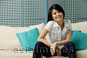 Asia Images Group - Young woman sitting on sofa, smiling at camera