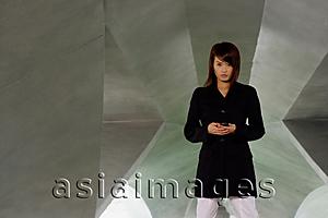 Asia Images Group - Woman in black jacket, holding phone, looking at camera