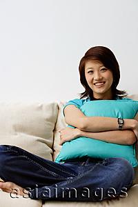 Asia Images Group - Woman sitting on sofa, hugging cushion, looking at camera