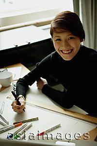 Asia Images Group - Female designer sitting at table with ruler and felt tip marker, smiling at camera