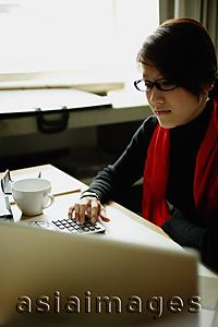 Asia Images Group - Woman sitting at desk with calculator and laptop