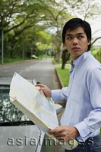 Asia Images Group - Man standing next to car, holding map, looking over shoulder