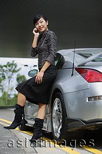 Asia Images Group - Woman leaning on car, using mobile phone