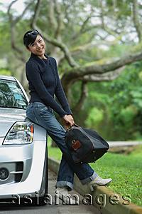 Asia Images Group - Woman holding bag, leaning on car, smiling at camera