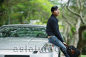 Asia Images Group - Woman holding bag, sitting on hood of car