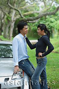 Asia Images Group - Couple looking at each other, man leaning on hood of car