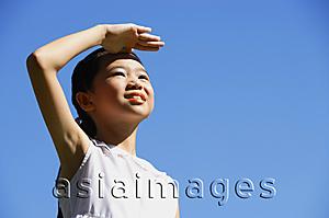 Asia Images Group - Girl standing outdoors, shielding eyes, looking away