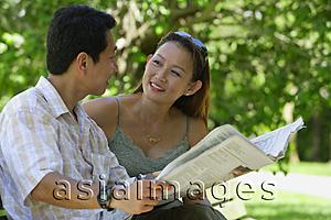 Asia Images Group - Couple sitting on bench, looking at each other, man holding newspaper