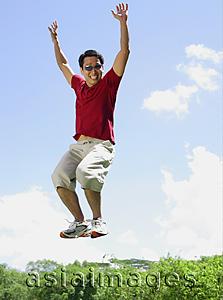 Asia Images Group - Man jumping in mid air, arms outstretched, smiling