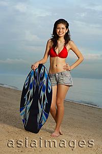 Asia Images Group - Young woman on beach, standing next to skimboard