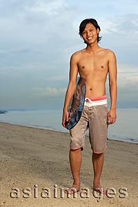 Asia Images Group - Young man holding skimboard, standing on beach